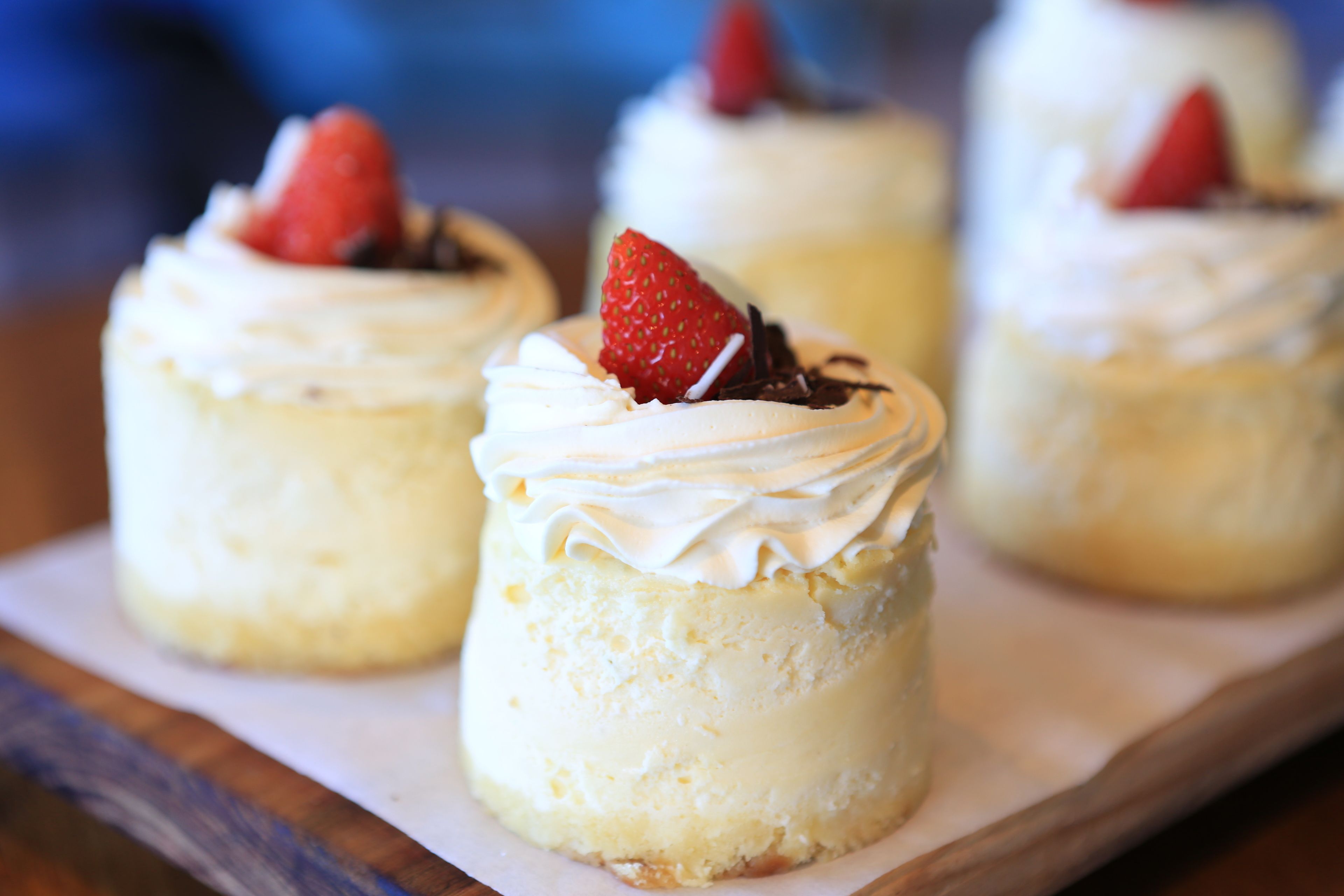 Tres mini cheesecakes con crema batida y fresas sobre una tabla de madera.