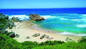 A beach with clear blue water, rocky outcrops, and greenery. - Brenton Haven Beachfront Resort (Knysna)