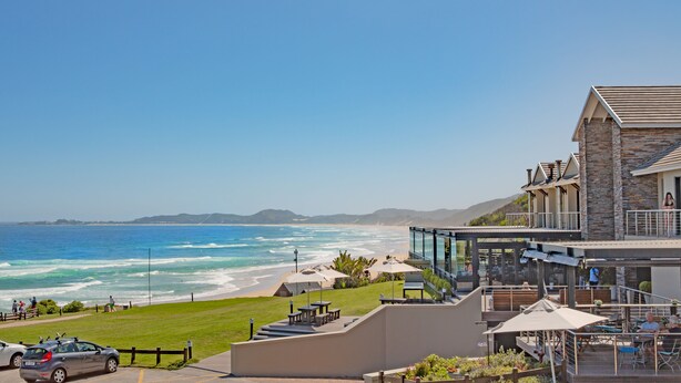 A coastal hotel with a view of the ocean, outdoor seating, and a stone facade. - Brenton Haven Beachfront Resort (Knysna)