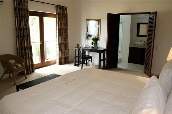 A hotel room with a large bed, a desk with a chair, a mirror, and a bathroom visible through an open door.