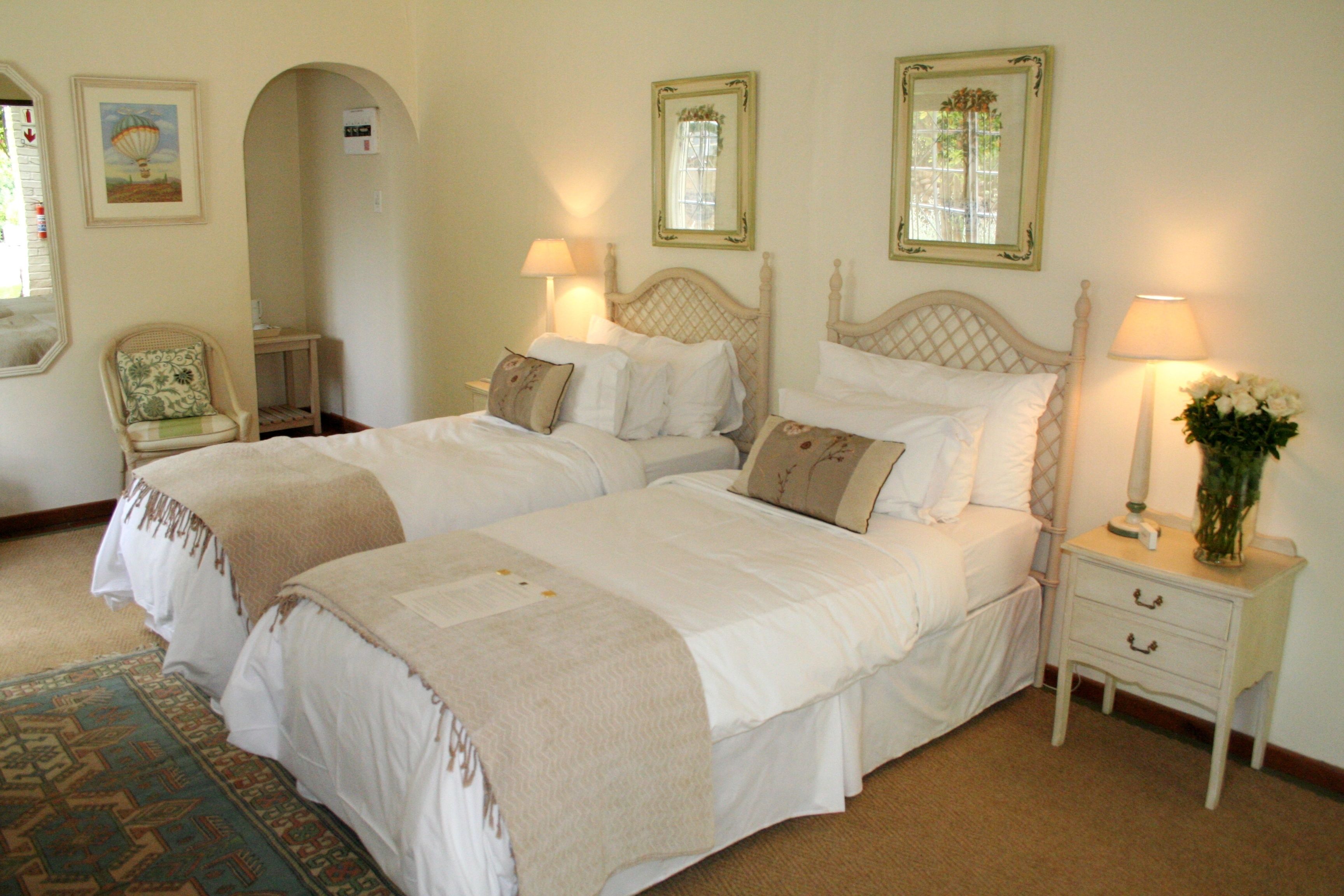 Une chambre avec deux lits, une table de chevet avec une lampe, une chaise et un miroir au mur.
