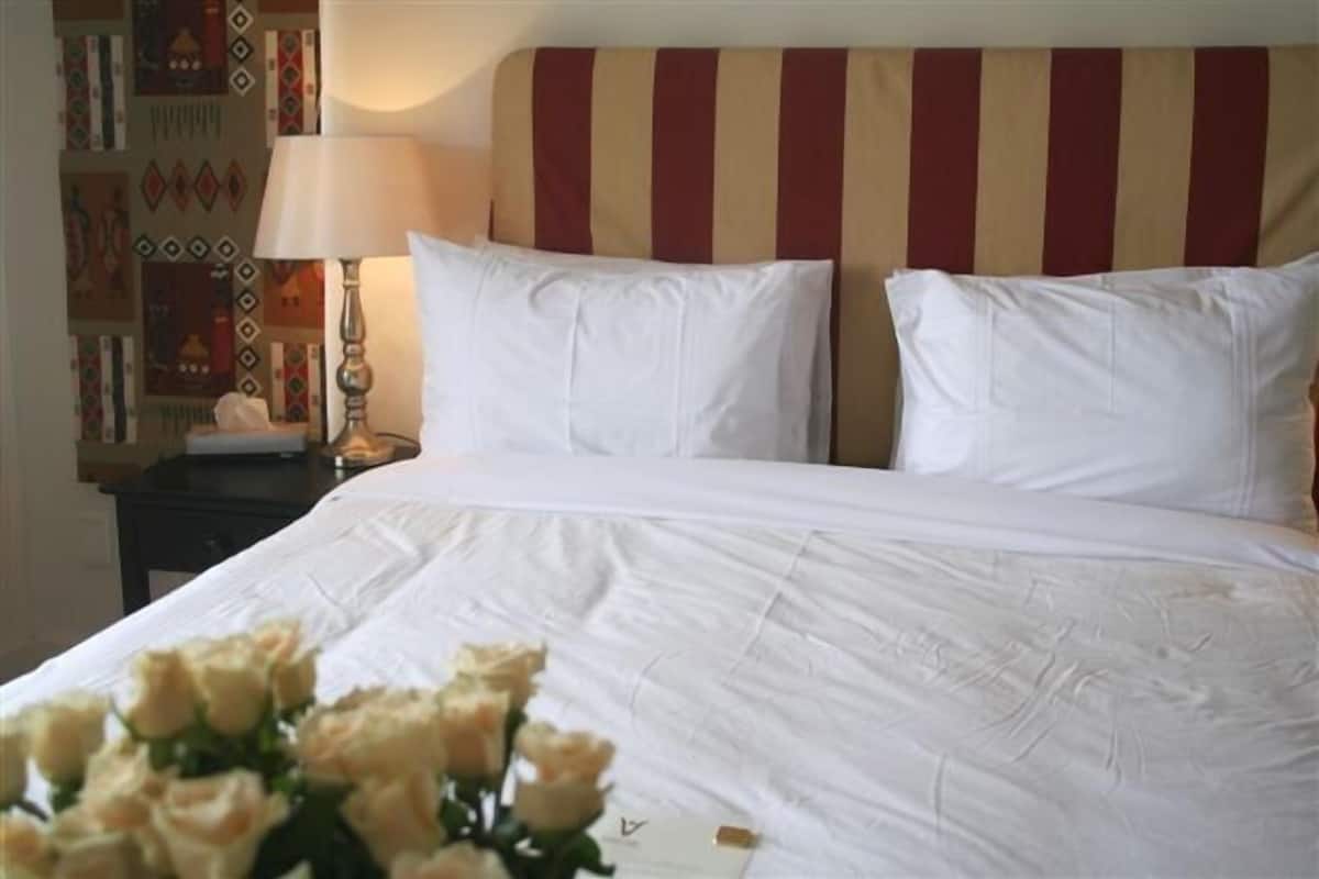 A neatly made bed with white linens, a striped headboard, and a bedside table with a lamp and a vase of flowers.