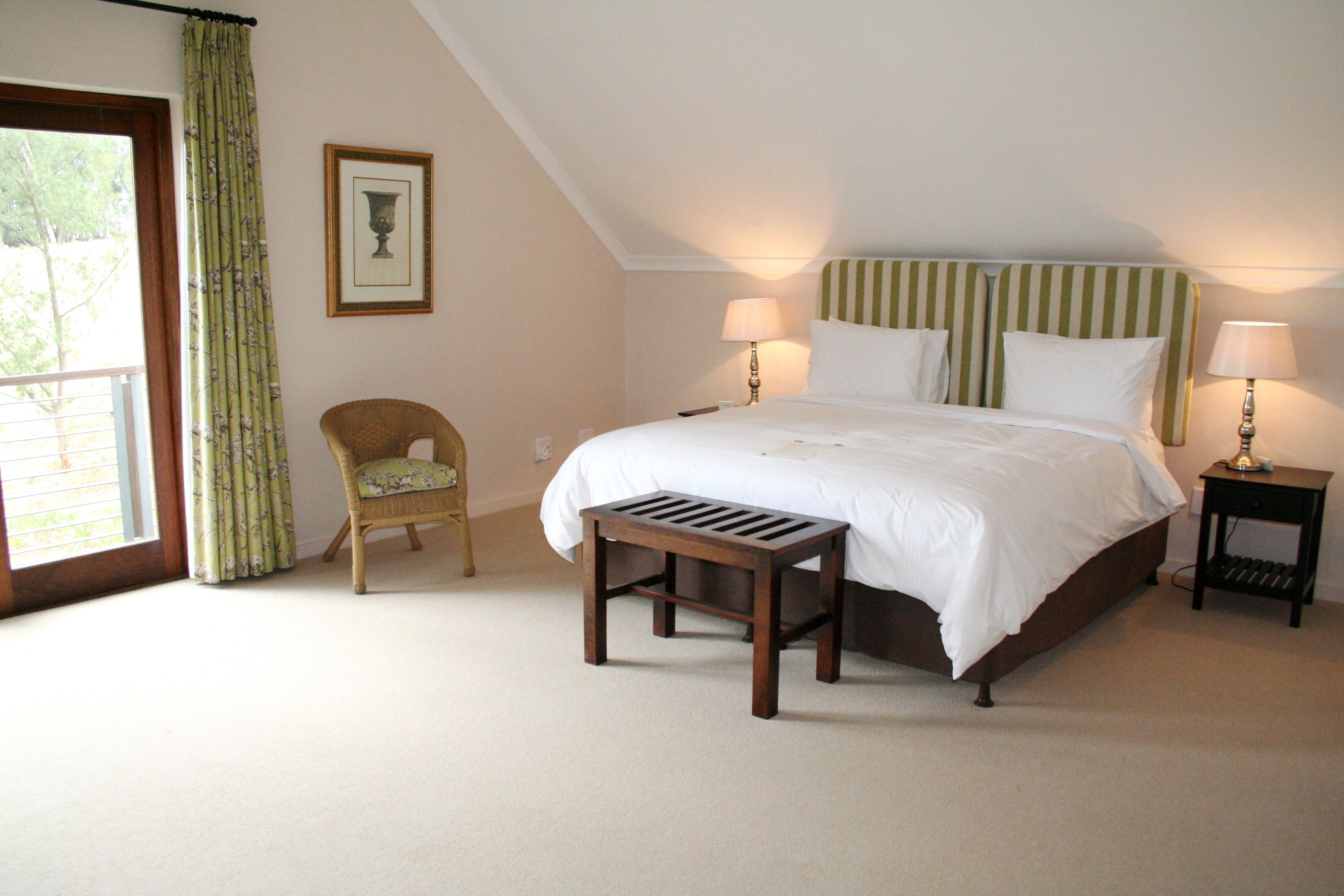 A bedroom with a bed, two bedside tables with lamps, a chair, a bench, a window with curtains, and a framed picture on the wall.