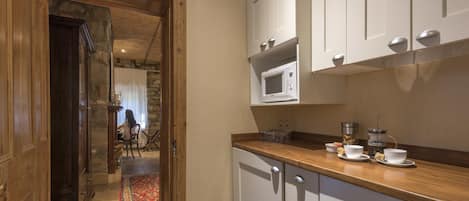 Una cocina con armarios blancos, encimera de madera y pared de piedra.