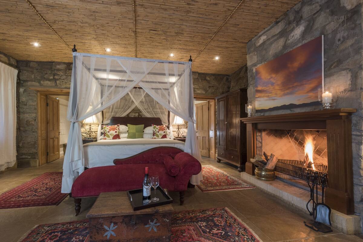 A bedroom with a four-poster bed, a fireplace, and a painting on the wall.