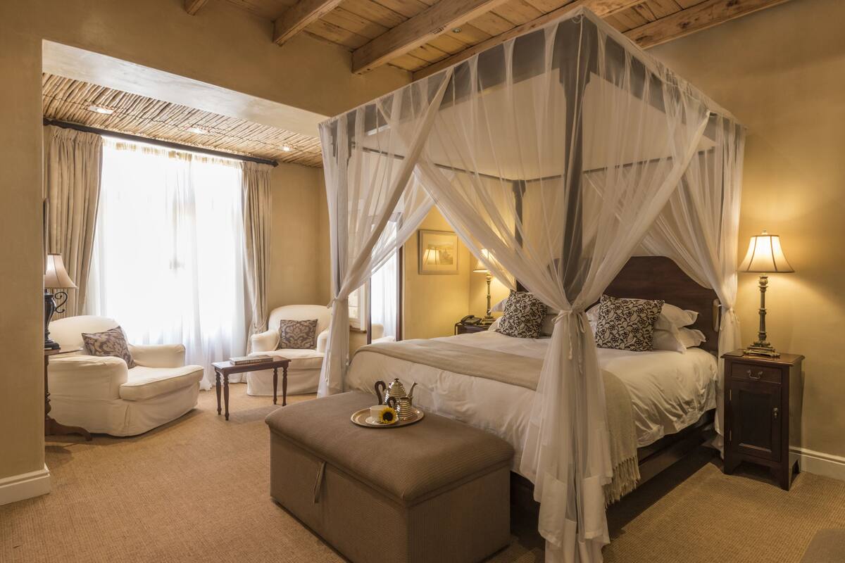 A four-poster canopy bed with a bedside table and lamp, a sofa, and a small ottoman with a tray.