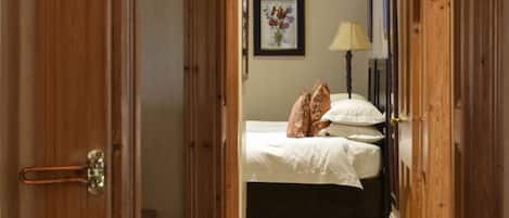 A narrow hallway leading to a bedroom with a bed, a nightstand, and a lamp.