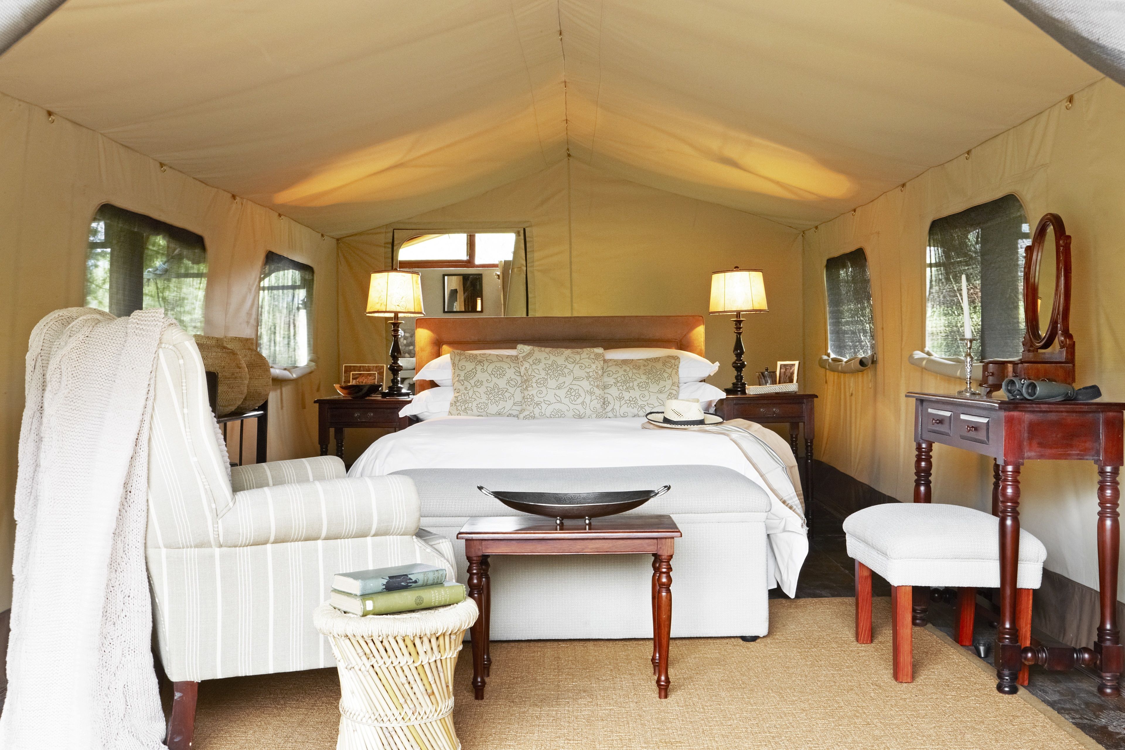 A tented room with a bed, bedside lamps, a mirror, a small table, and a chair.