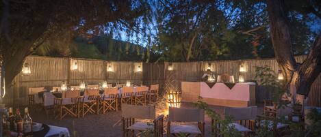 An outdoor dining area with wooden tables and chairs, a buffet table, and a fire pit.