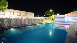 A swimming pool with a decorative fence and a building with multiple windows in the background. - Lilypool - The Heritage Jalmahal (Jaipur)