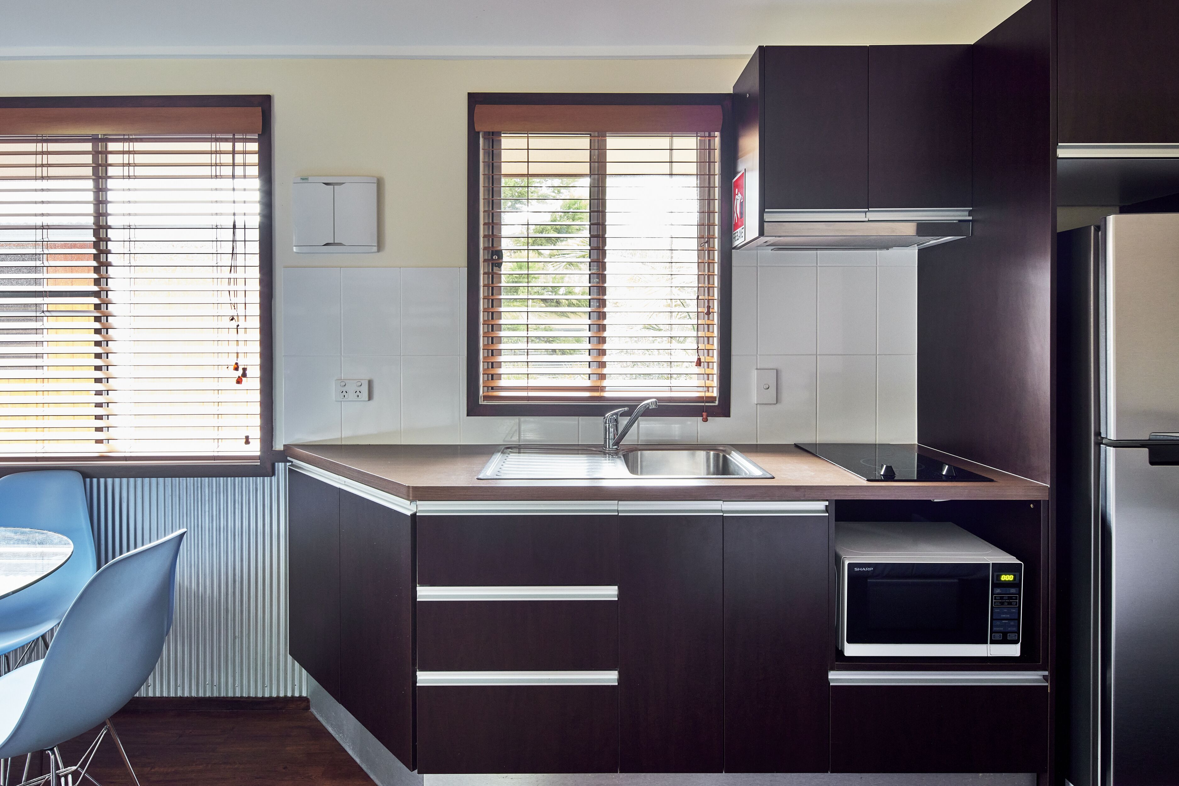 A modern kitchen with dark cabinetry, a stainless steel sink, a built-in microwave, and a window with blinds.
