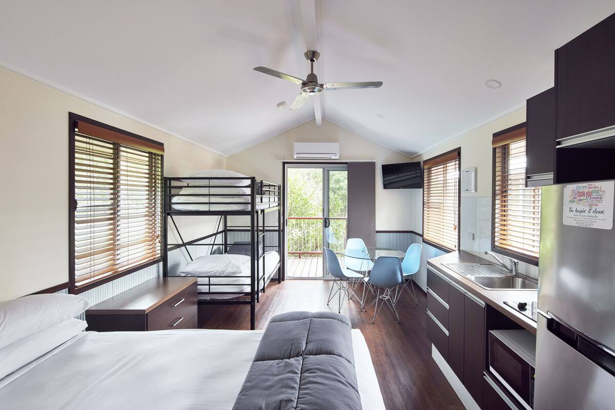 A compact hotel room with bunk beds, a kitchenette, a dining area, and a balcony.