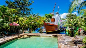 Un complexe hôtelier tropical doté d’une piscine, de chaises longues et d’un grand bateau.