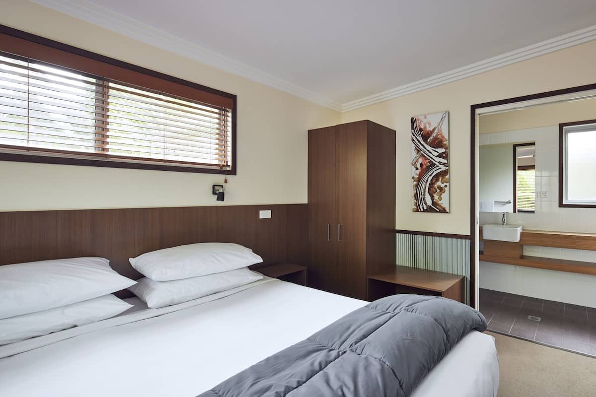 A bedroom with a bed, a wardrobe, a bedside table, and a bathroom visible through an open door.