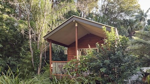 Un kiosque en bois doté d’un toit incliné, entouré d’une végétation luxuriante et d’arbres.