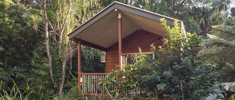 A wooden gazebo with a sloped roof, surrounded by dense foliage and trees.