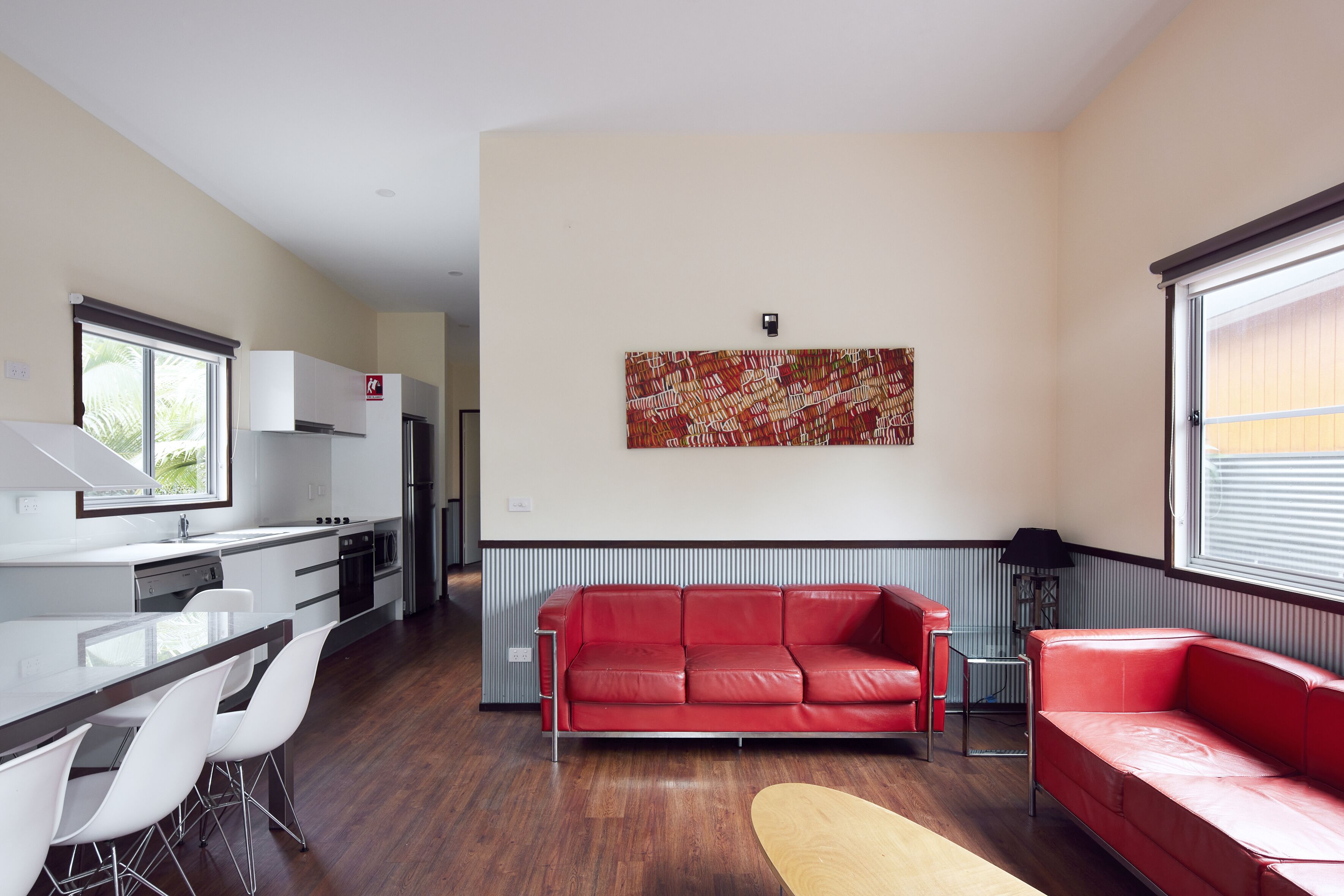 A modern kitchen with white cabinets, a red leather sofa, and a dining area with white chairs.