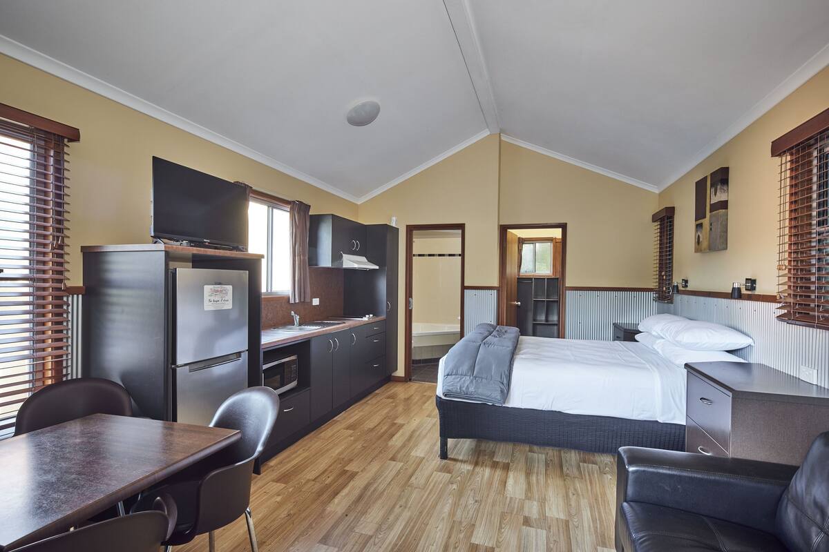 A compact room with a bed, a desk, a chair, a kitchenette, and a bathroom.