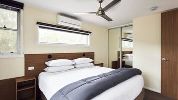 A neatly arranged bedroom with a bed, bedside tables, a ceiling fan, an air conditioning unit, and a window.