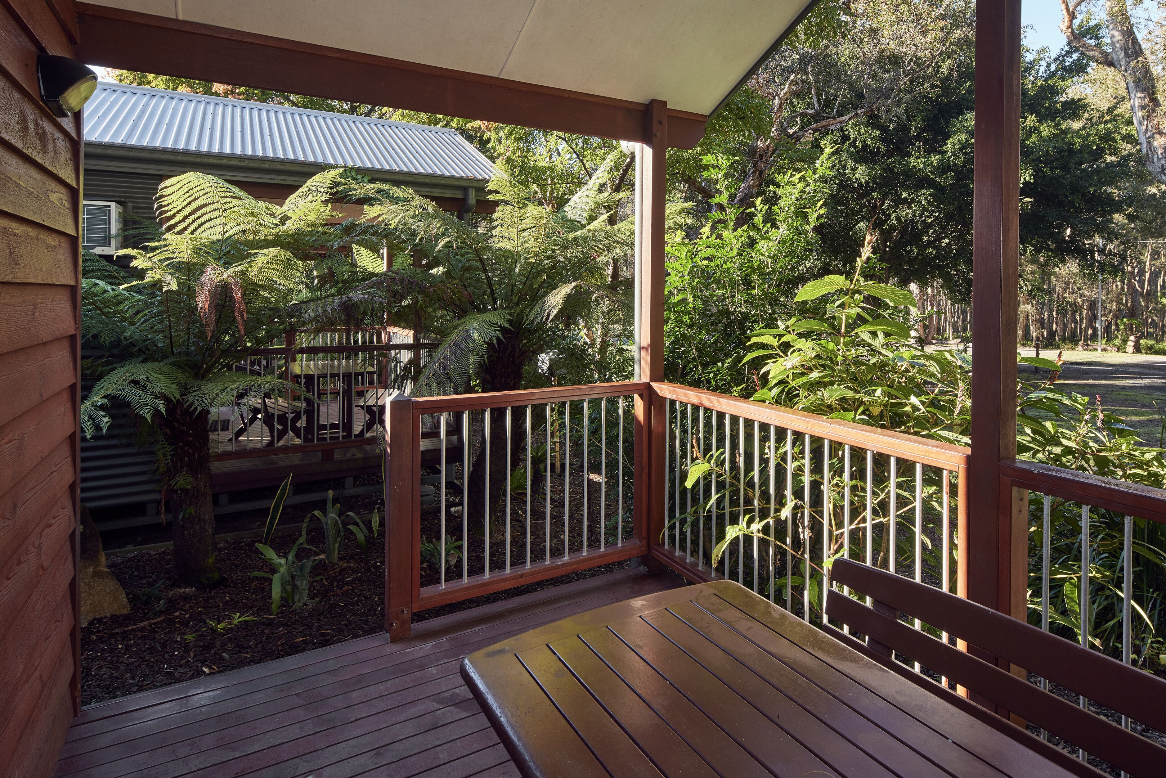 Une terrasse en bois avec un banc, entourée d’une végétation luxuriante et agrémentée d’une rambarde en métal.