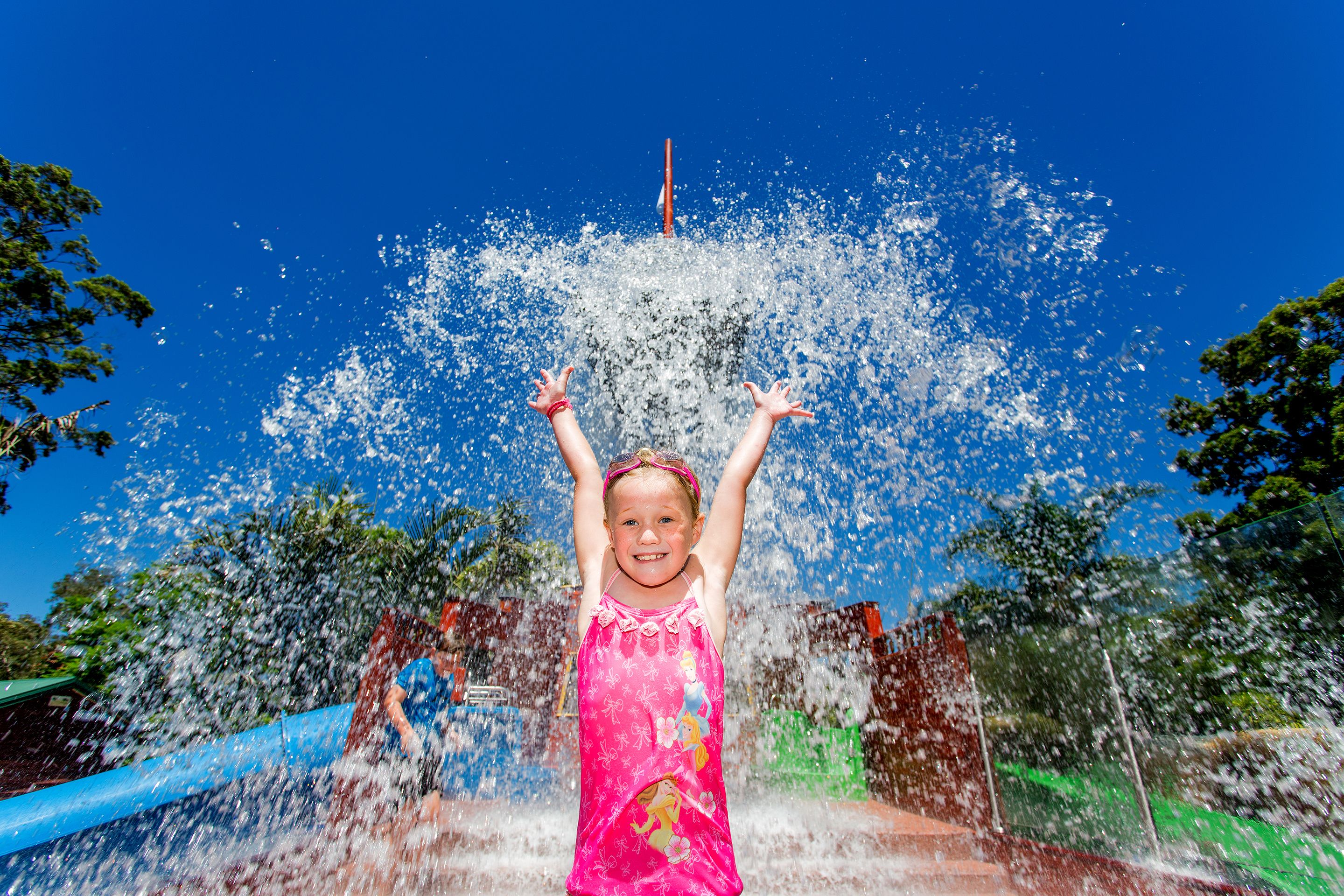 Ein Kind in einem rosafarbenen Kleid spielt mit Wasserspielen in einem Park.
