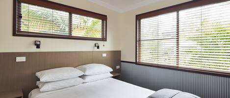 A neatly made bed with white and gray bedding, a wooden headboard, and a window with blinds.
