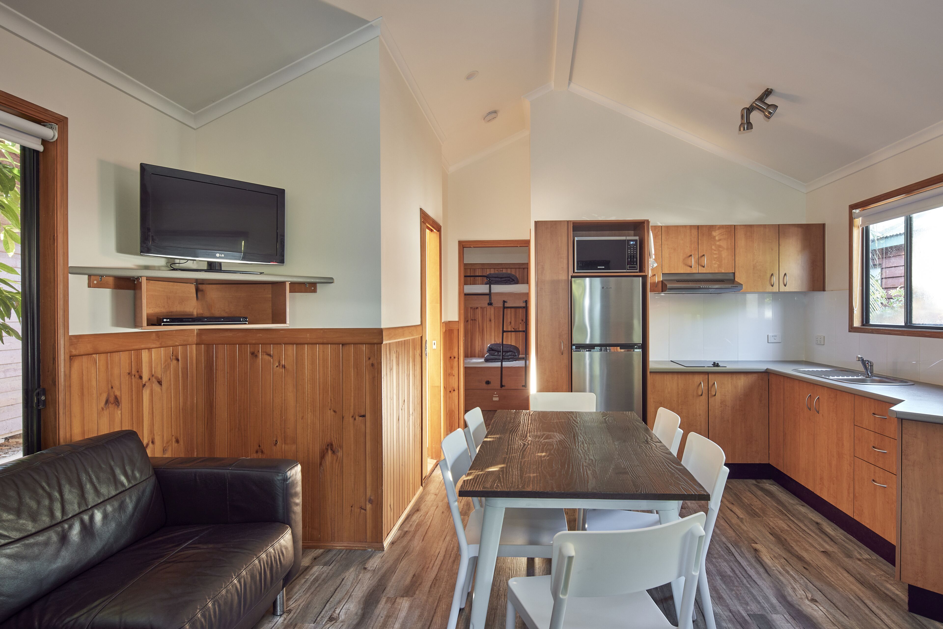 Eine moderne Küche mit Holzausstattung, einem Edelstahlkühlschrank und einem eingebauten Ofen. Es gibt einen Essbereich mit einem Holztisch und weißen Stühlen.