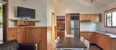 Eine moderne Küche mit Holzausstattung, einem Edelstahlkühlschrank und einem eingebauten Ofen. Es gibt einen Essbereich mit einem Holztisch und weißen Stühlen.