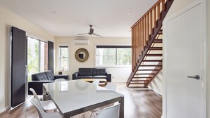 Un salon moderne comprenant une table à manger, deux canapés, un escalier et un ventilateur de plafond.