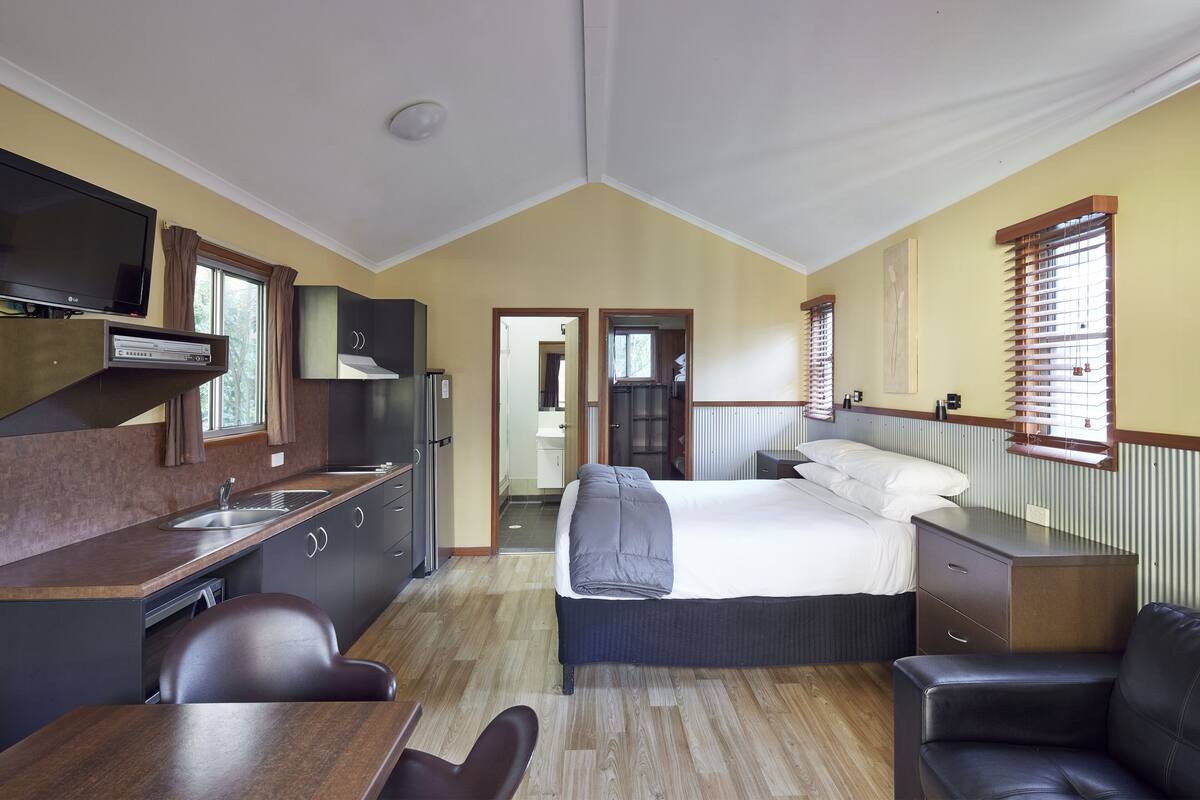 A compact room with a kitchenette, a bed, a desk, and a chair.