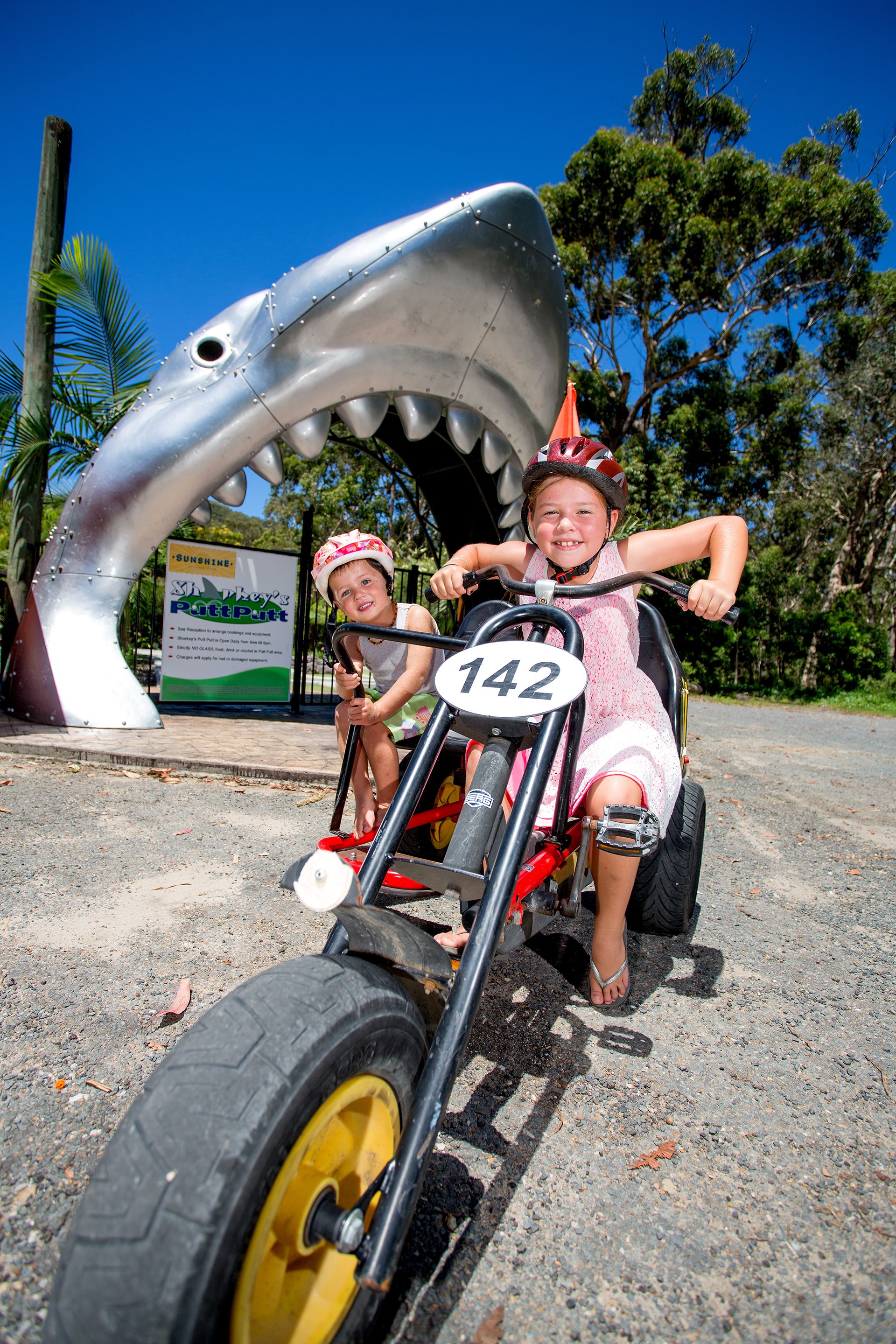 A child on a tricycle with a shark decoration.