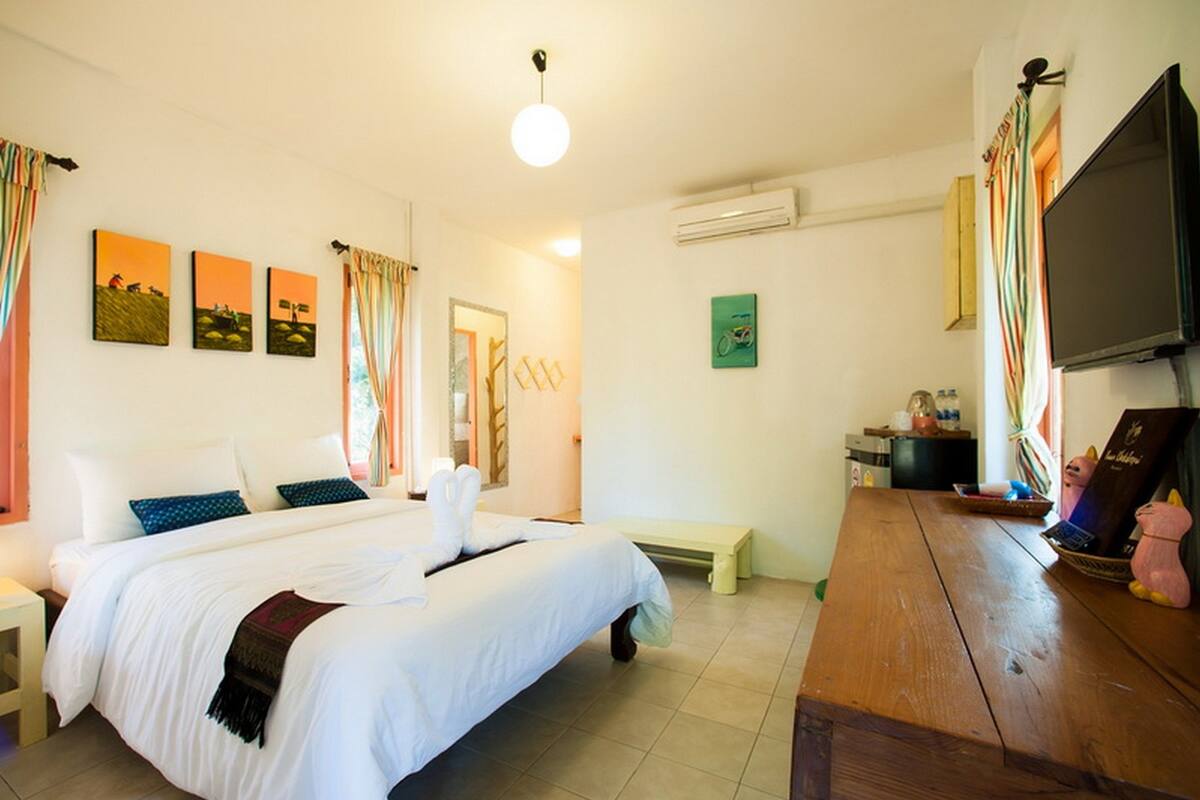 Habitación de hotel con cama, mesitas de noche, un escritorio de madera, televisor y obras de arte en las paredes.