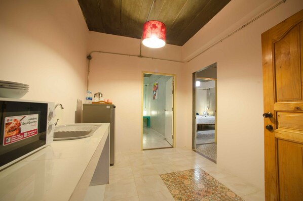A kitchen with a microwave, sink, and cabinets. There is a wooden door on the right and a hallway leading to another room. - Baan Chokdee Pai Resort (Pai)