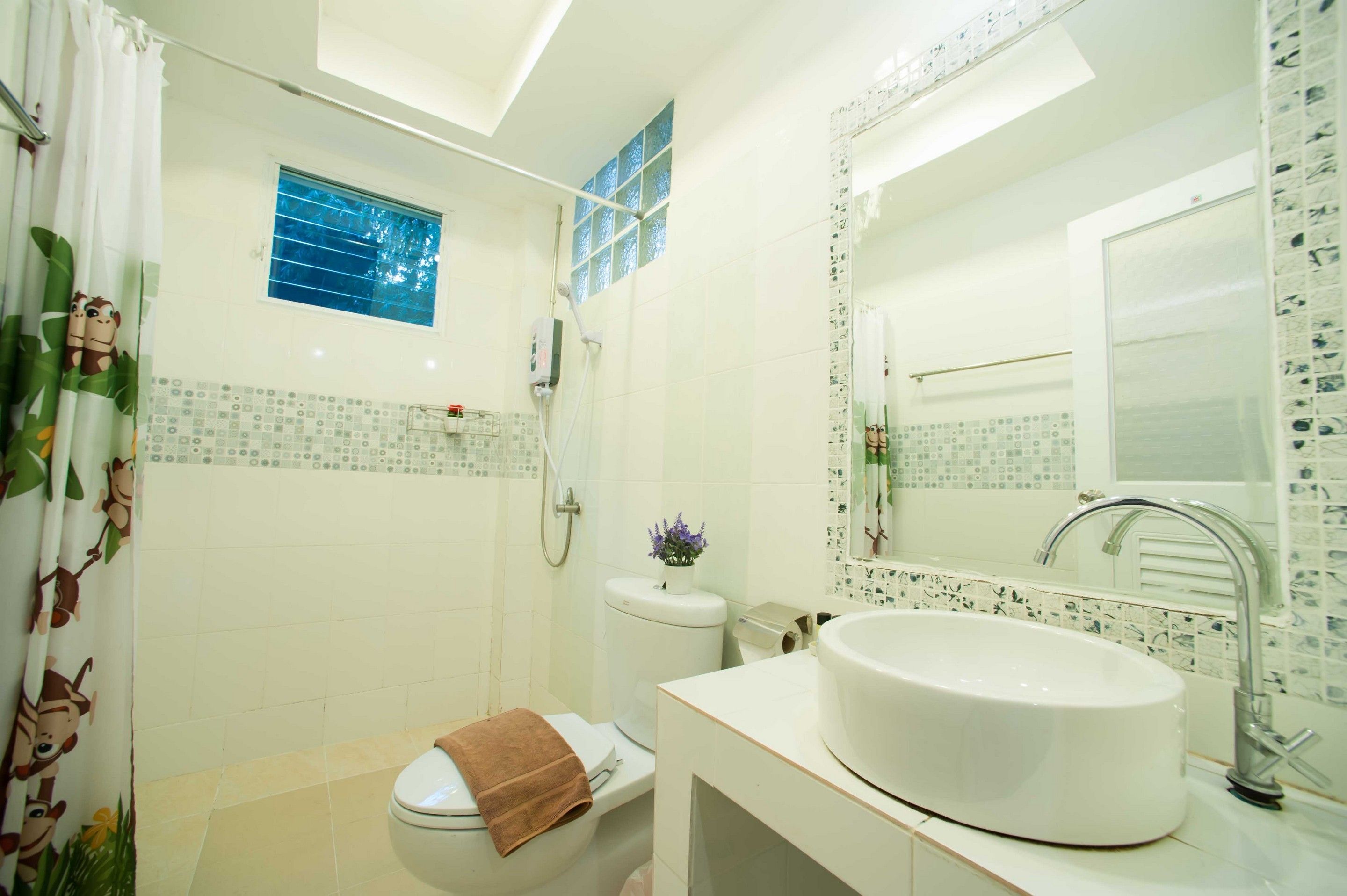A bathroom with a toilet, shower, sink, and a window.