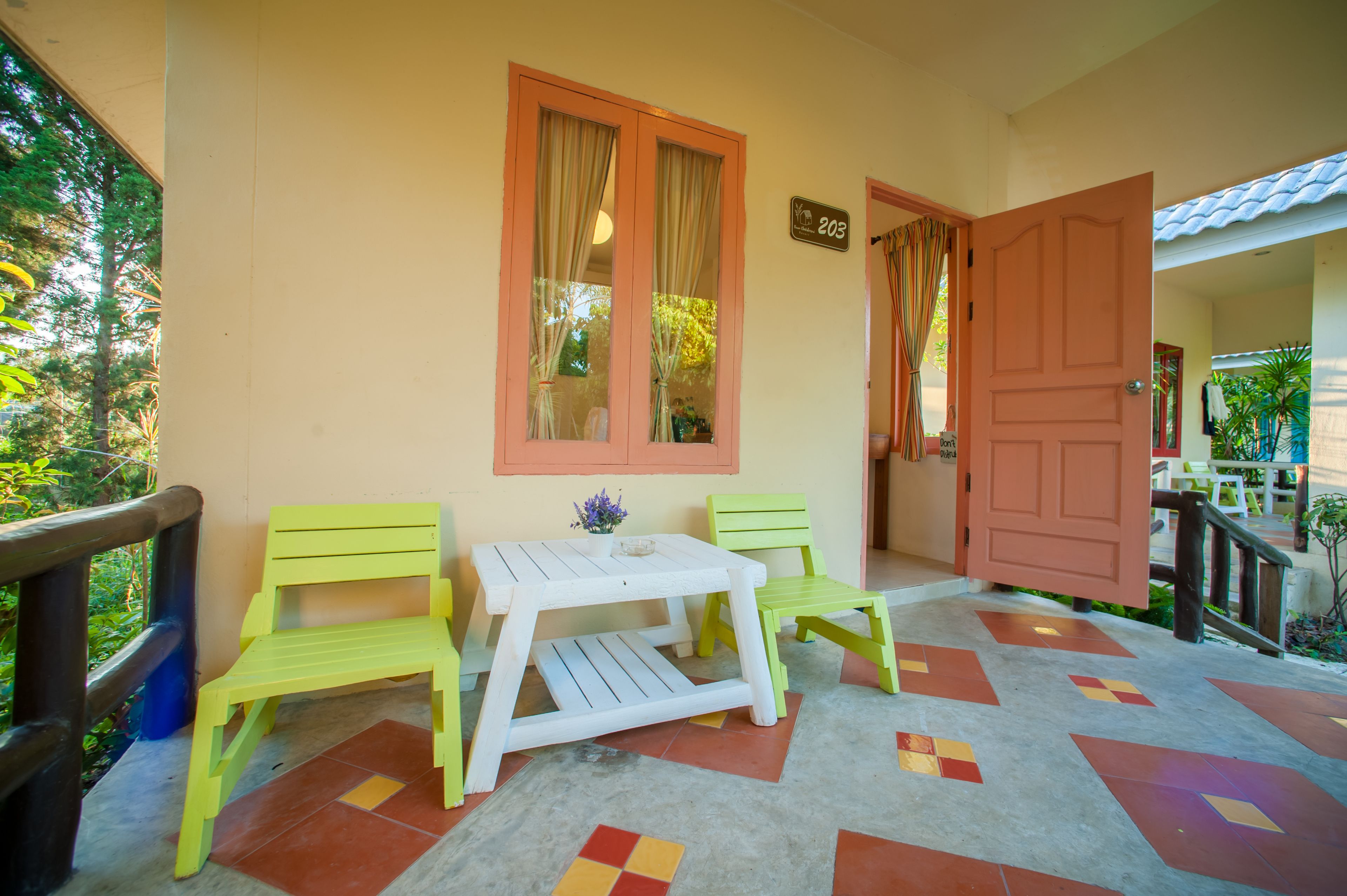 A room with a white table and two green chairs, a wooden door, and a window with curtains.