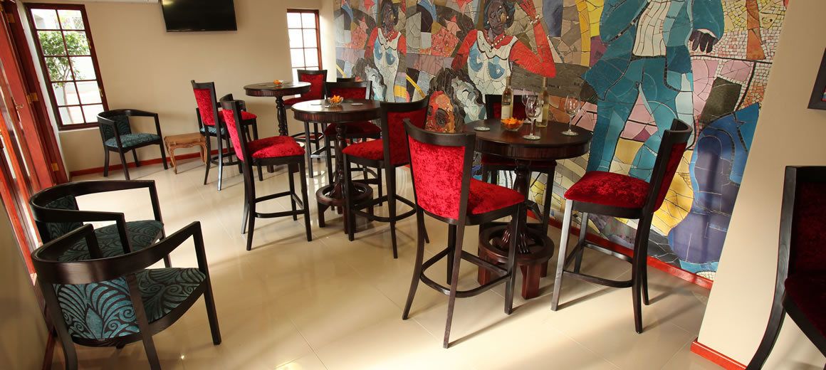 A dining area with multiple tables and chairs, some with red cushions. There is a large, colorful abstract mural on the wall.