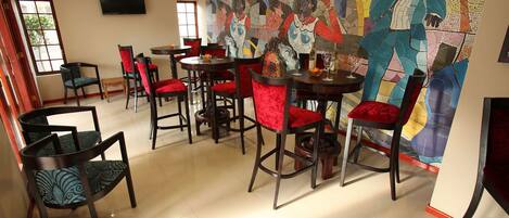 A dining area with multiple tables and chairs, some with red cushions. There is a large, colorful abstract mural on the wall.