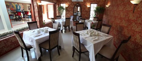 Un restaurante con mesas redondas dispuestas para comer, sillas y un espejo grande en la pared.