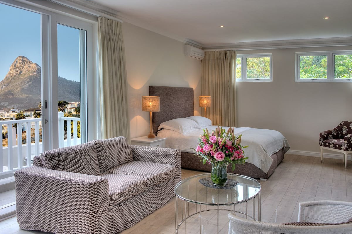 Ein Hotelzimmer mit Bett, einer Couch, einem kleinen Tisch mit Blumenvase und einem Balkon mit Bergblick.