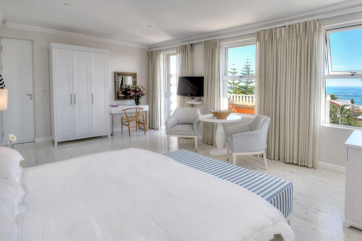 Ein Hotelzimmer mit einem großen Bett, einem Schreibtisch mit Stuhl, einem kleinen runden Tisch mit zwei Stühlen, einem Fernseher und Meerblick.