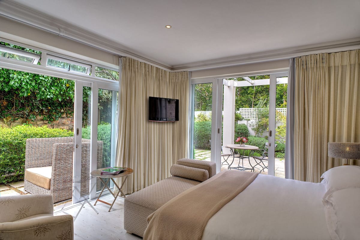 Ein geräumiges Schlafzimmer mit einem großen Bett, einem Fernseher und Blick auf einen Garten durch Glastüren.