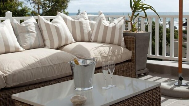A wicker sofa with striped cushions, a glass table with two wine glasses and a pitcher, and a view of the ocean. - Sea Five Boutique Hotel (Cape Town)