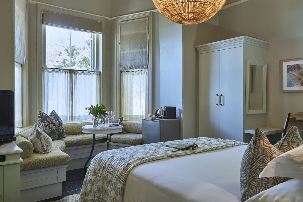A hotel room with a bed, seating area, TV, and a small table with a plant.