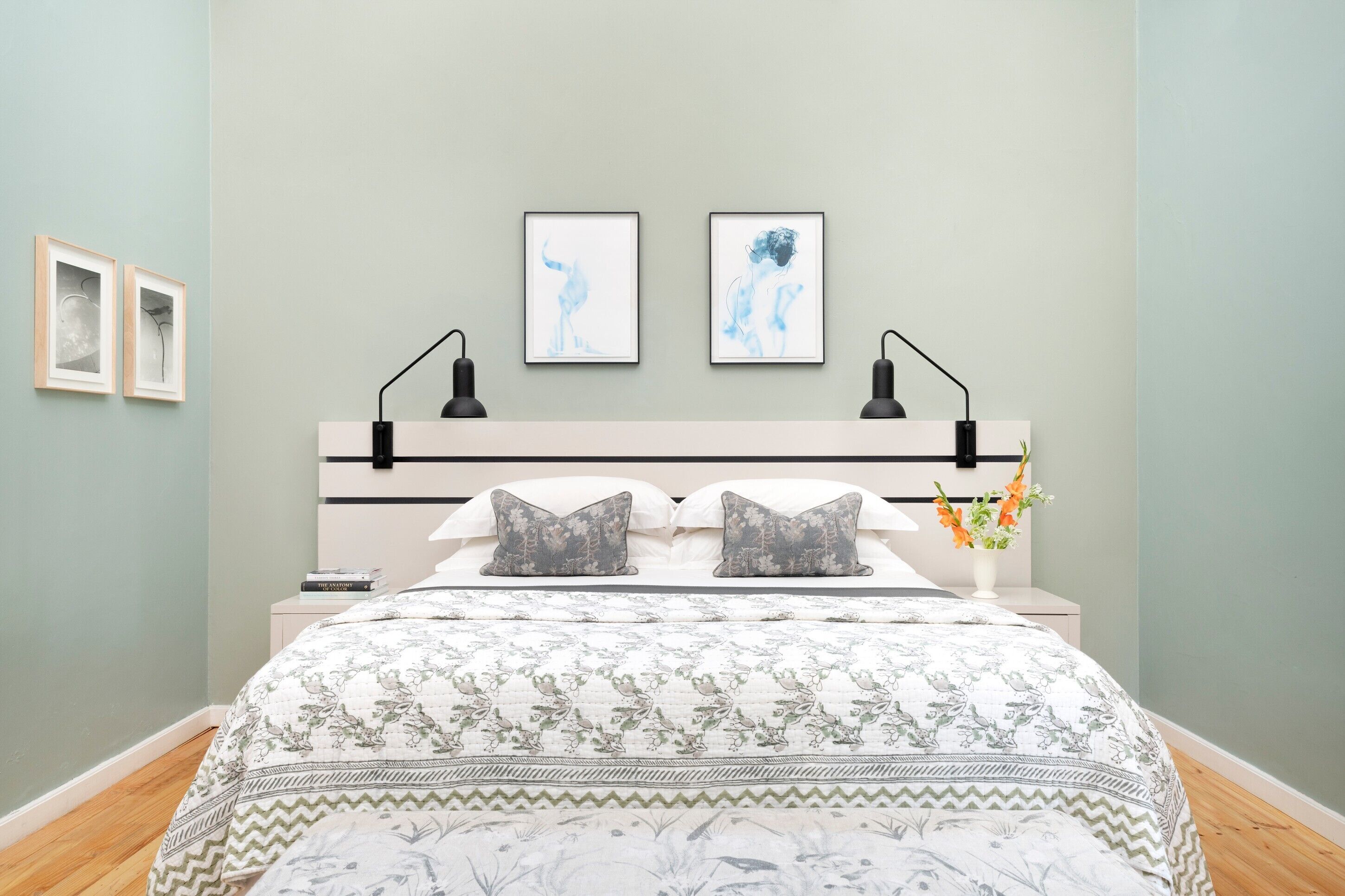 A bedroom with a bed, bedside tables, a nightstand, wall art, and a vase with flowers.
