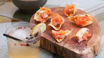 A table with a glass of white wine, a bowl of nuts, and a wooden board with salmon appetizers.