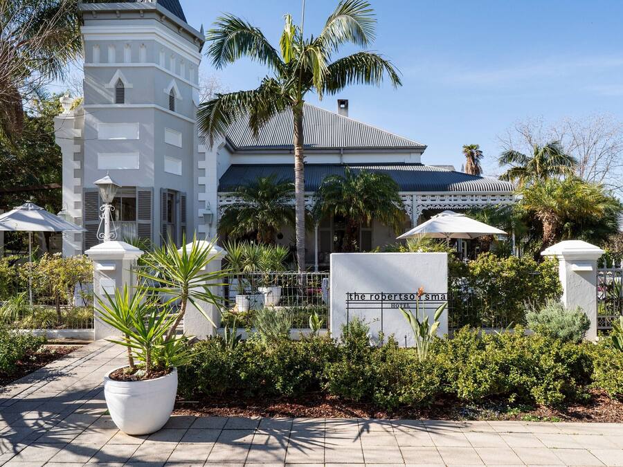 A hotel entrance with a sign reading "The Robertson's Hotel," surrounded by palm trees and a paved walkway.