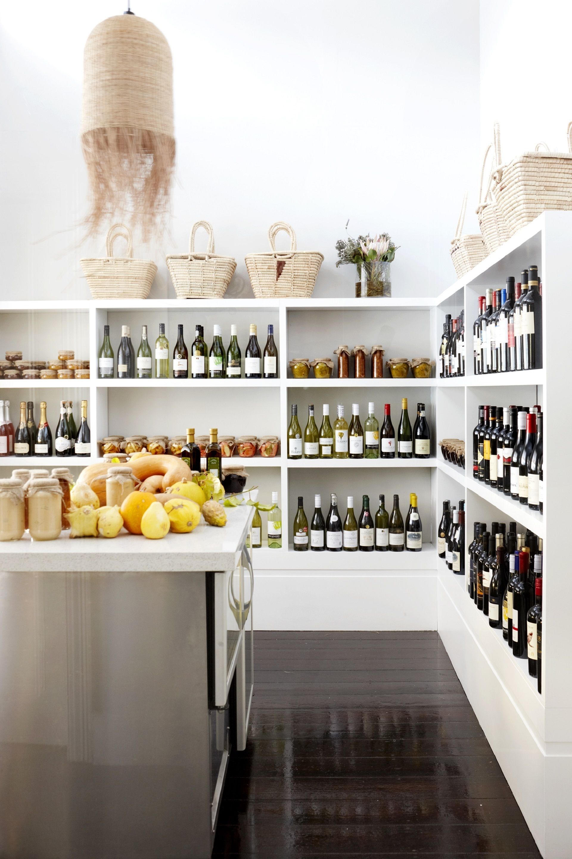 A wine cellar with shelves of wine bottles, baskets, and jars of food.