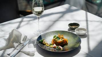 Une table à manger avec une assiette de nourriture, un verre de vin blanc et un bol de sel.