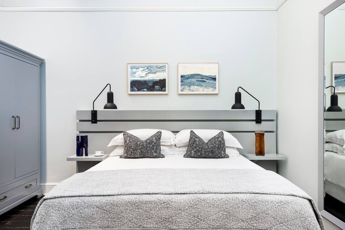 A modern bedroom with a bed, bedside tables, and artwork on the wall.