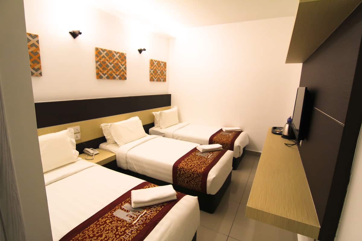 A hotel room with three single beds, a wooden desk, a TV, and a wall-mounted phone.